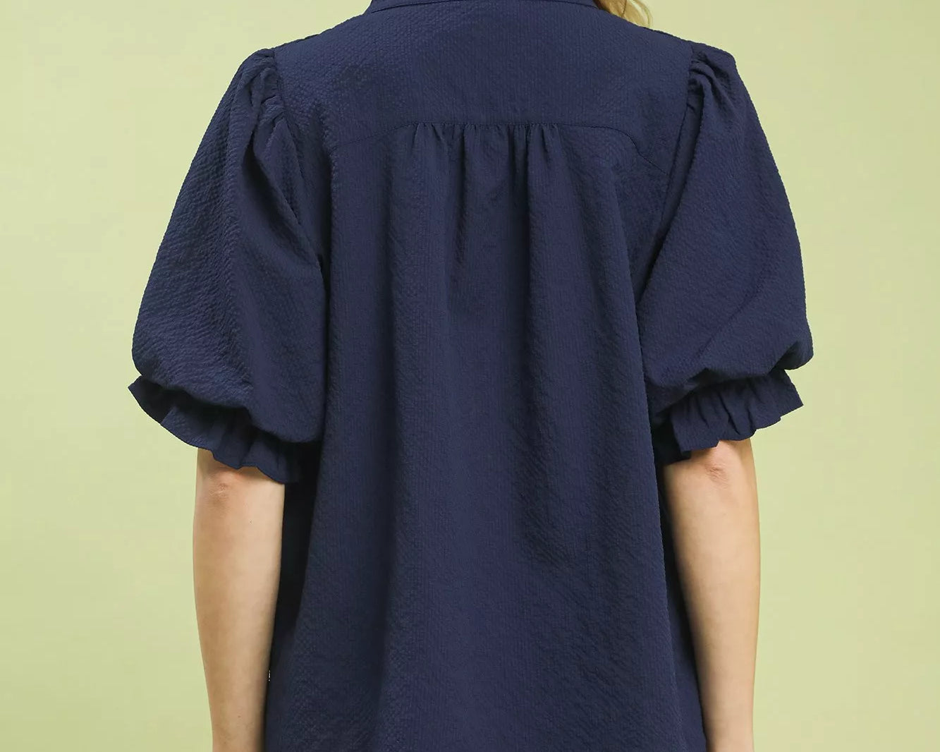 NEWYORKLISTED STYLE COLLECTION: Woman wearing a navy blue blouse with puffed sleeves on a light green background