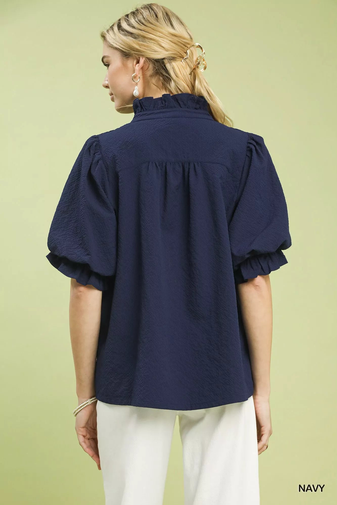 NEWYORKLISTED STYLE COLLECTION: Woman wearing a navy blue blouse with puffed sleeves on a light green background