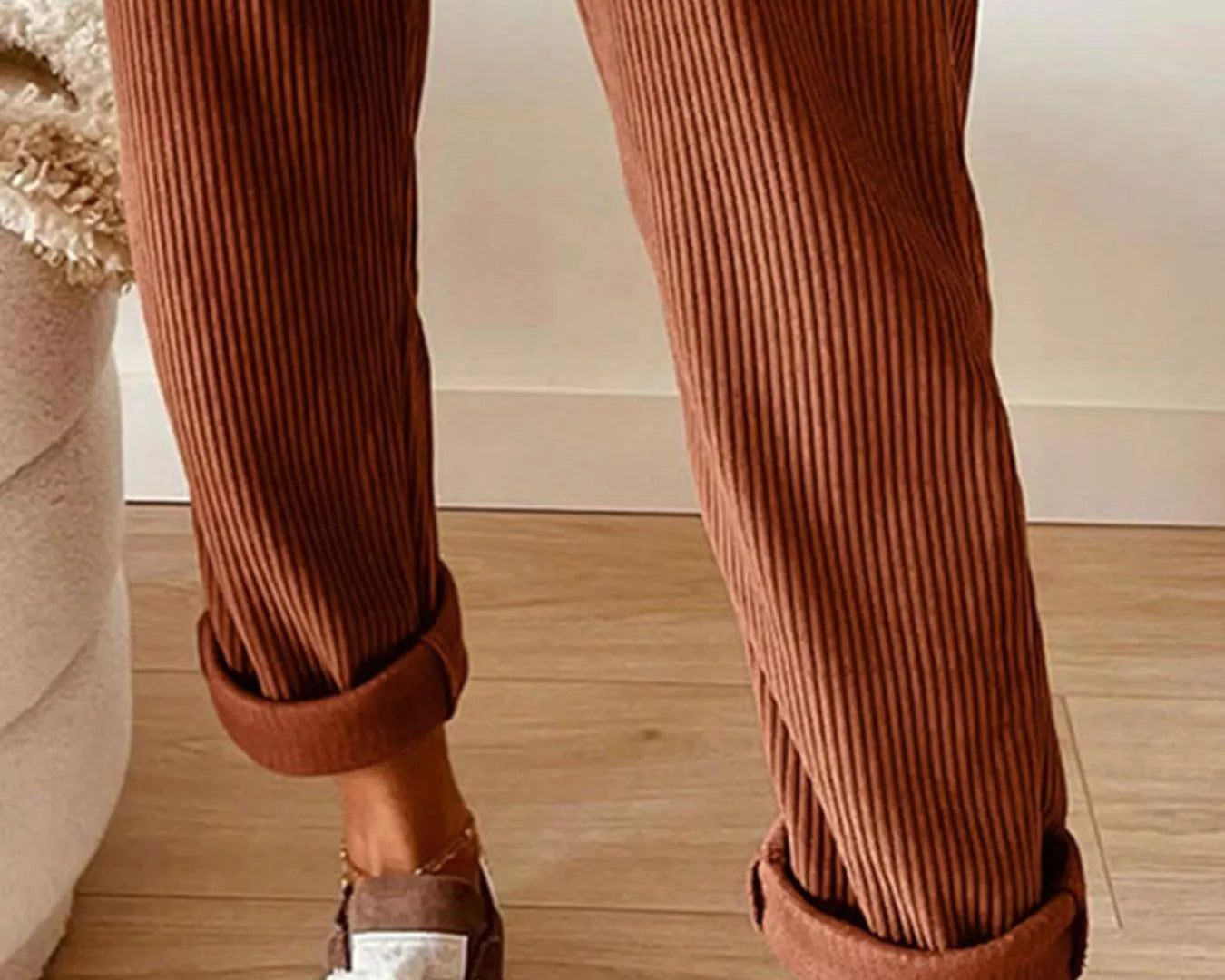Brown ribbed pants with white sneakers on a wooden floor.
