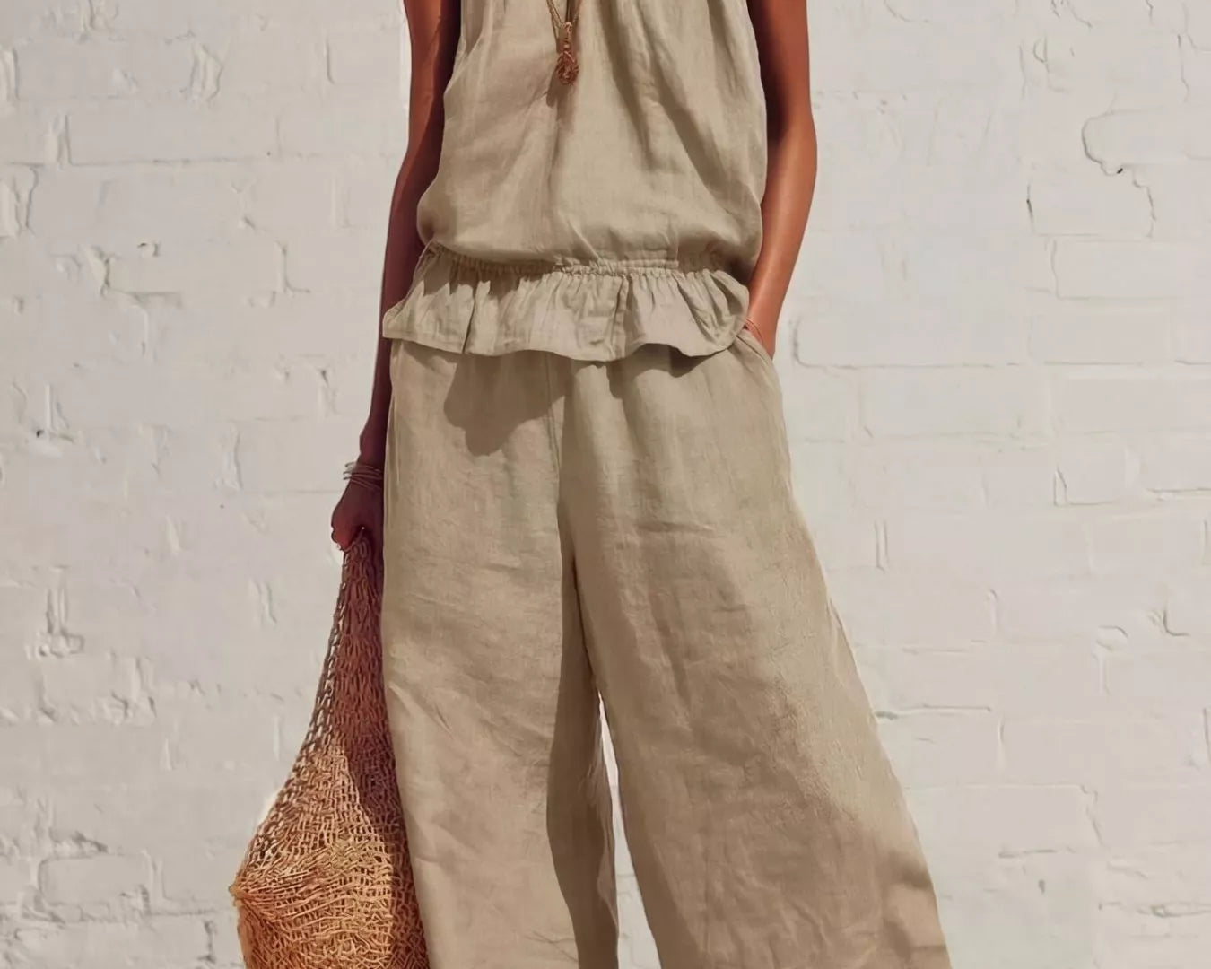 NEWYORKLISTED STYLE COLLECTION: Woman wearing a beige sleeveless top and wide-leg pants against a white brick wall.