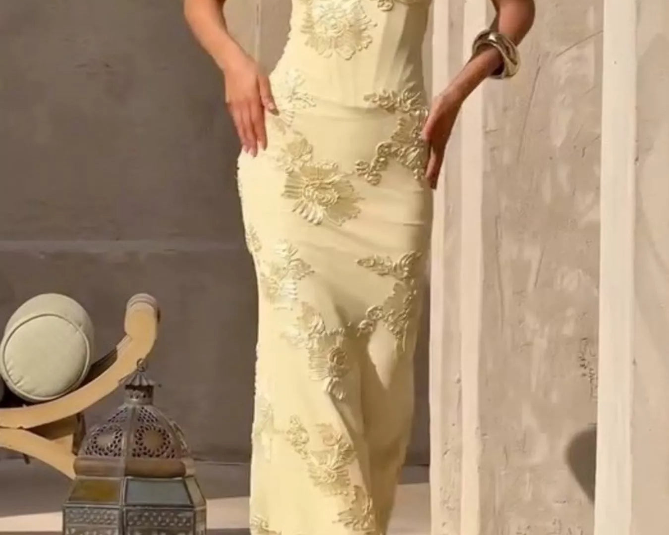 NEWYORKLISTED STYLE COLLECTION: Woman in a light yellow evening gown standing against a neutral wall with decorative elements.