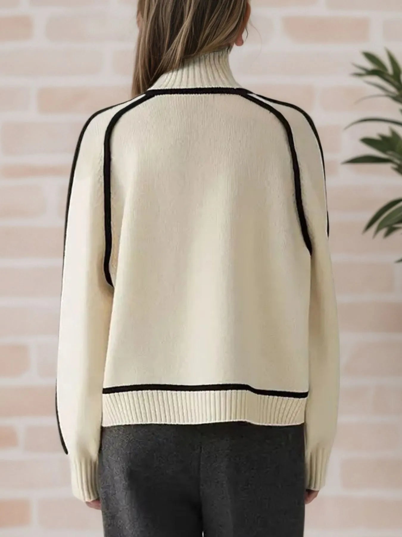 NEWYORKLISTED STYLE COLLECTION: Beige sweater with black trim worn by a person against a brick wall.