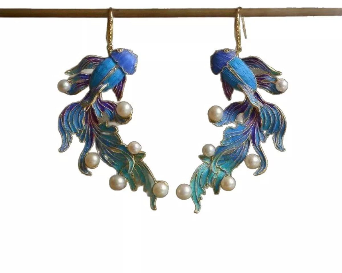NYLD GLAMOUR By NEWYORKLISTED: Pair of fish-shaped earrings with enamel details and pearl accents on a white background