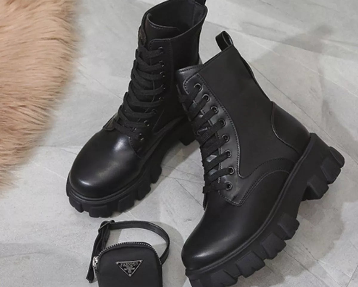 NEWYORKLISTED SHOE COLLECTION: Pair of black leather boots with a small black Prada bag on a light wooden floor.
