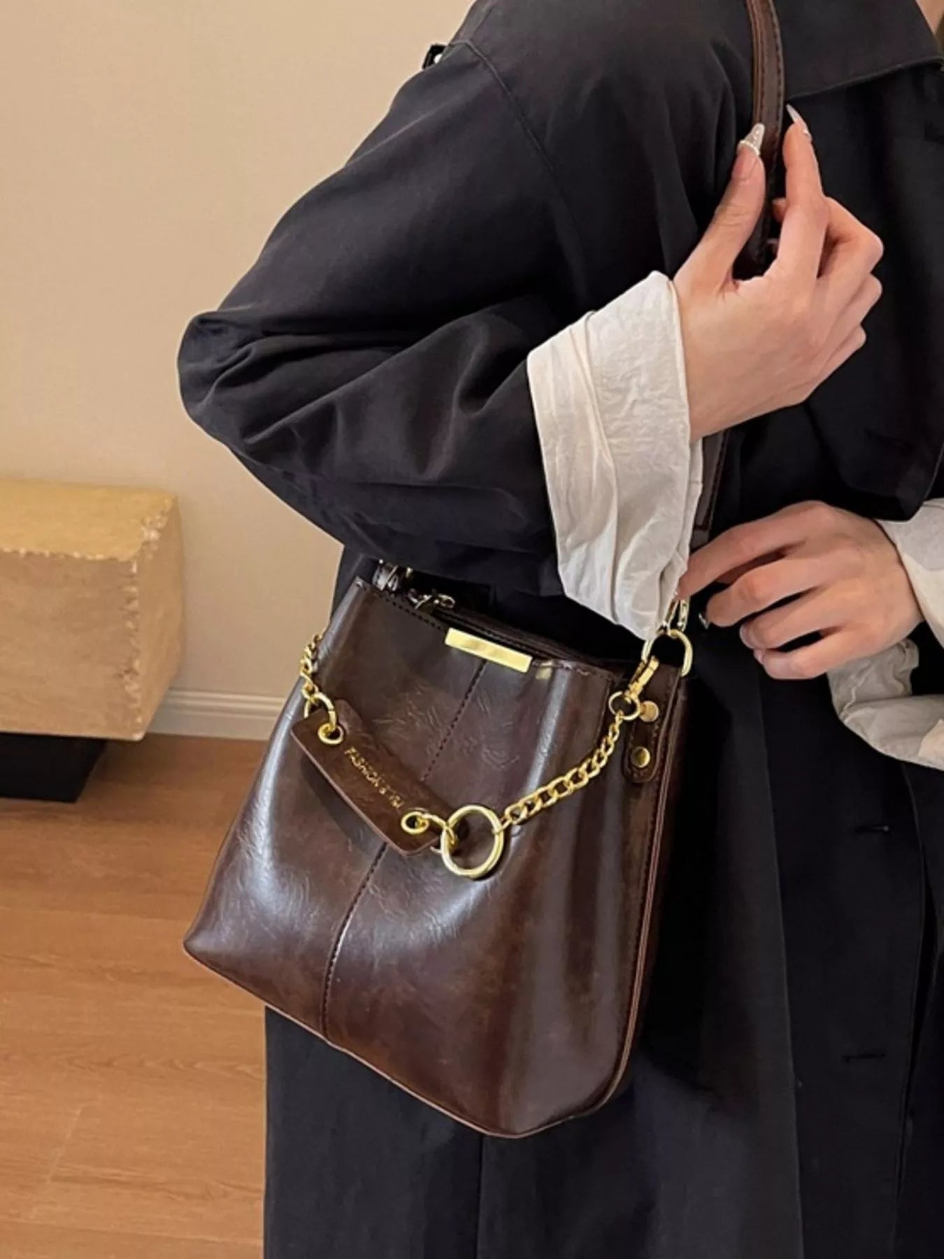 Person holding a brown leather handbag with gold chain detail indoors. New York Listed Style Collection