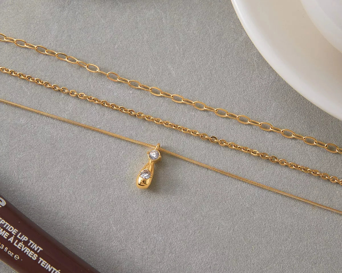 NYLD Glamour Collection by NEWYORKLISTED: Two gold necklaces on a gray surface with a white plate in the background.