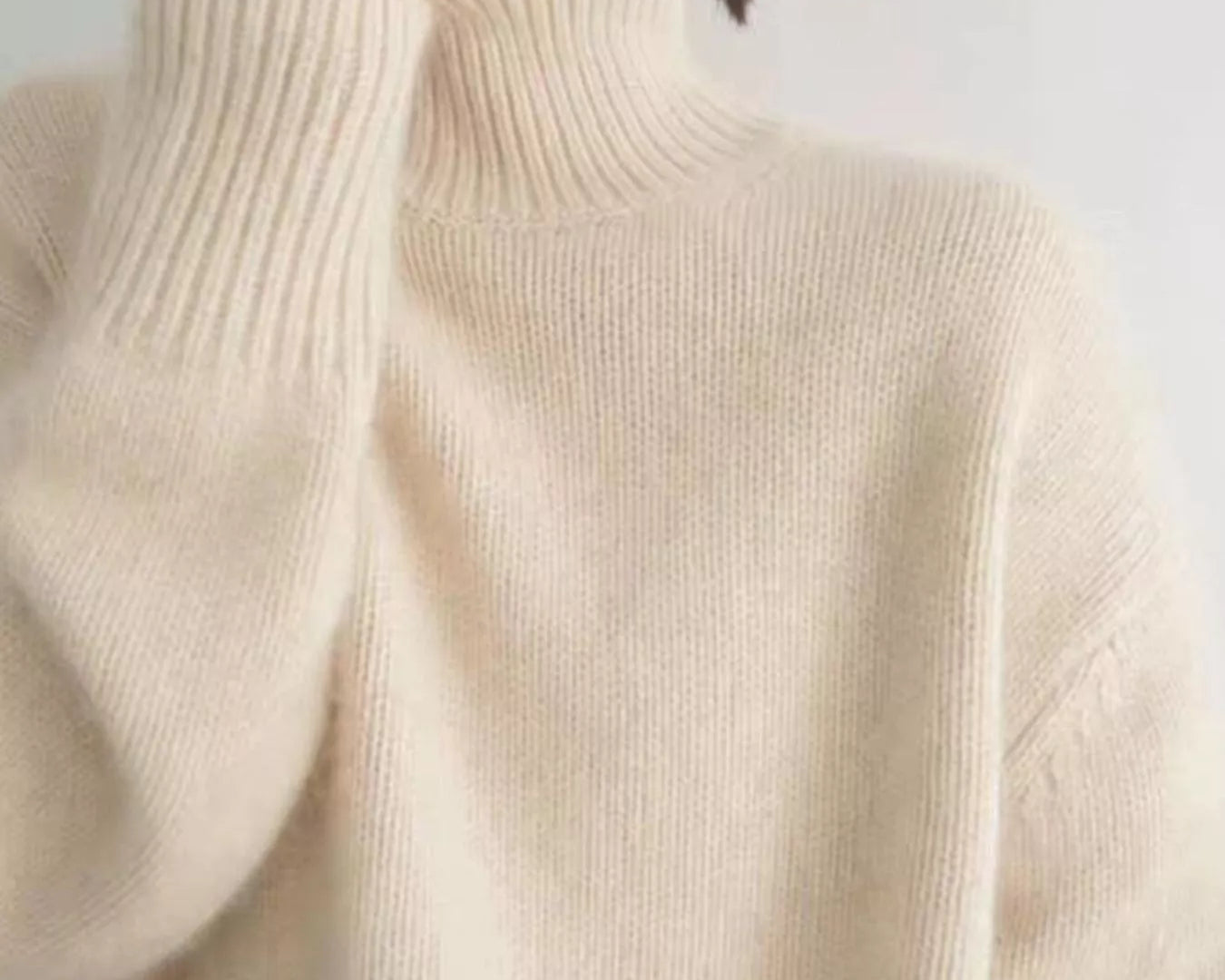 Close-up of a person wearing a beige turtleneck sweater against a plain background: NEWYORKLISTED STYLE COLLECTION