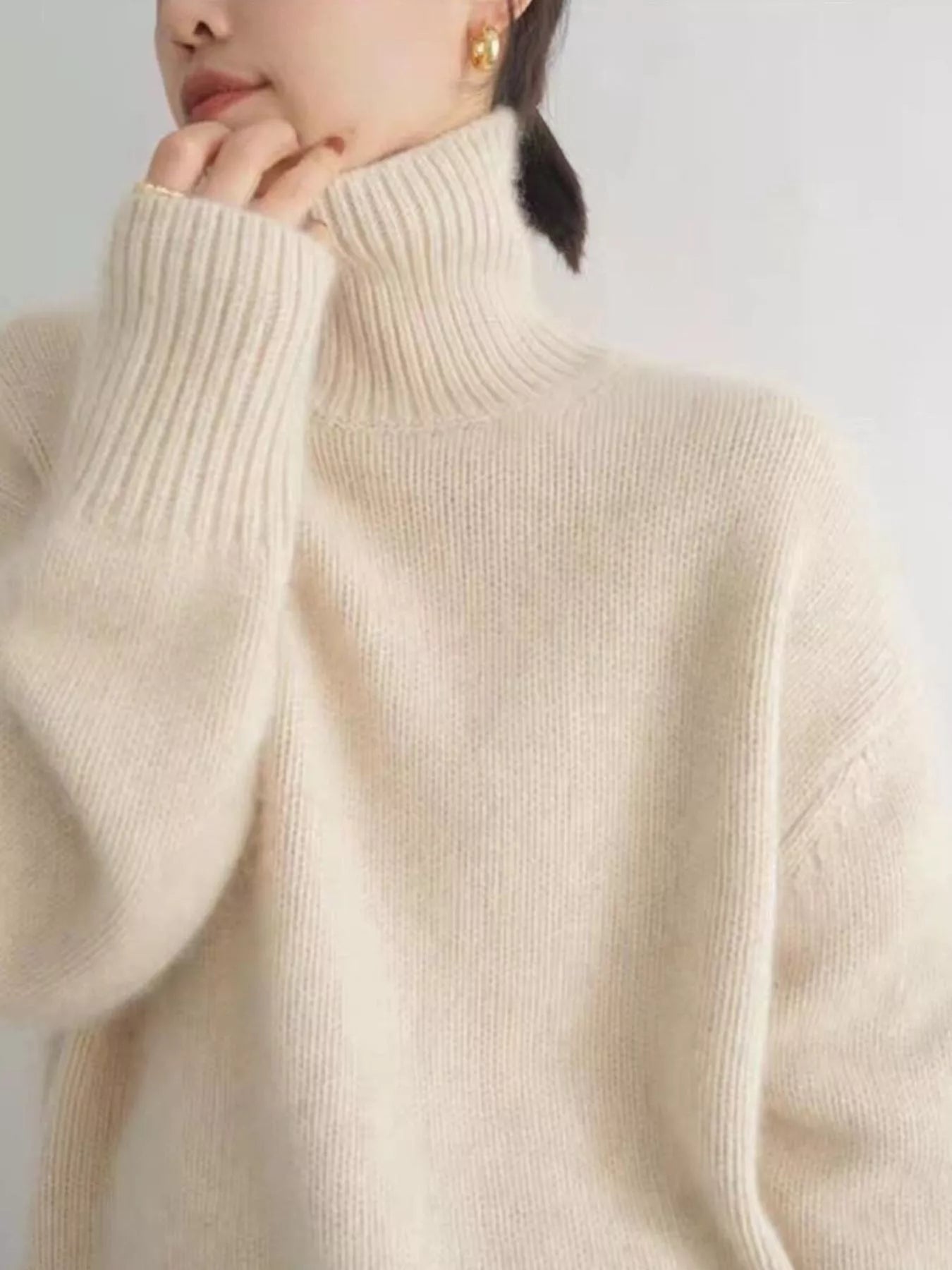 Close-up of a person wearing a beige turtleneck sweater against a plain background: NEWYORKLISTED STYLE COLLECTION