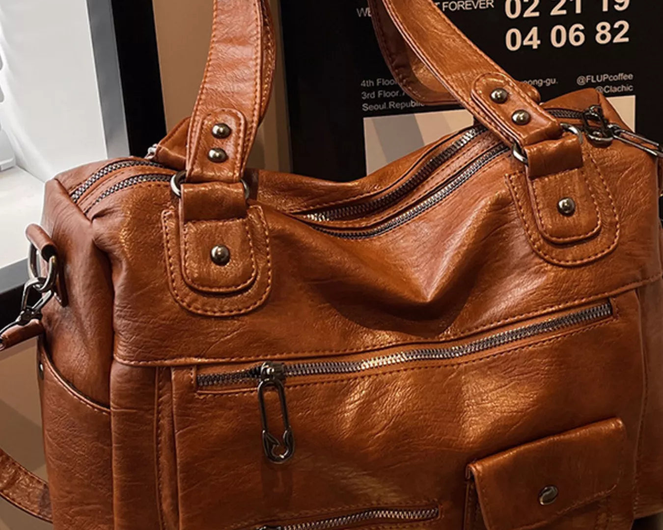 NEWYORKLISTED STYLE COLLECTION: Brown leather handbag on a surface with a blurred background