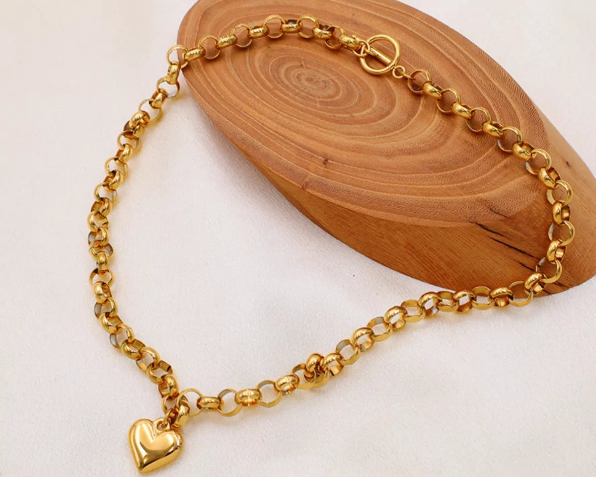 NYLD Glamour Collection by NEWYORKLISTED: Gold chain bracelet with a heart charm on a wooden block
