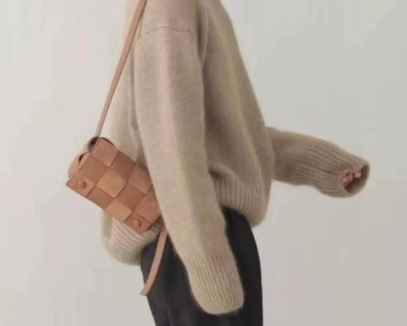 Person wearing a beige sweater holding a brown bag against a white background