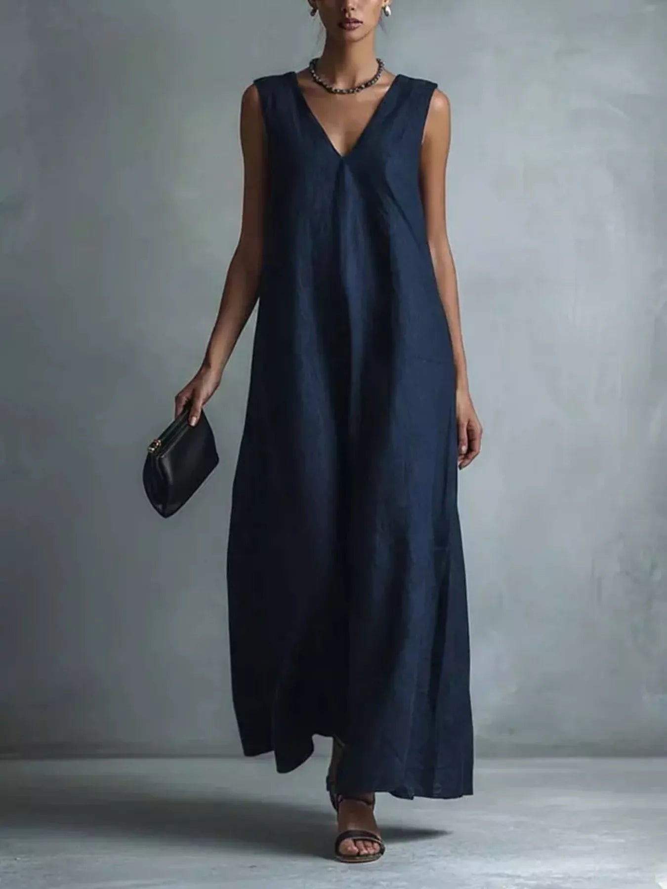 NEWYORKLISTED STYLE COLLECTION: A woman models a sleeveless navy blue maxi dress with a V-neckline, holding a small black clutch against a textured gray studio background.