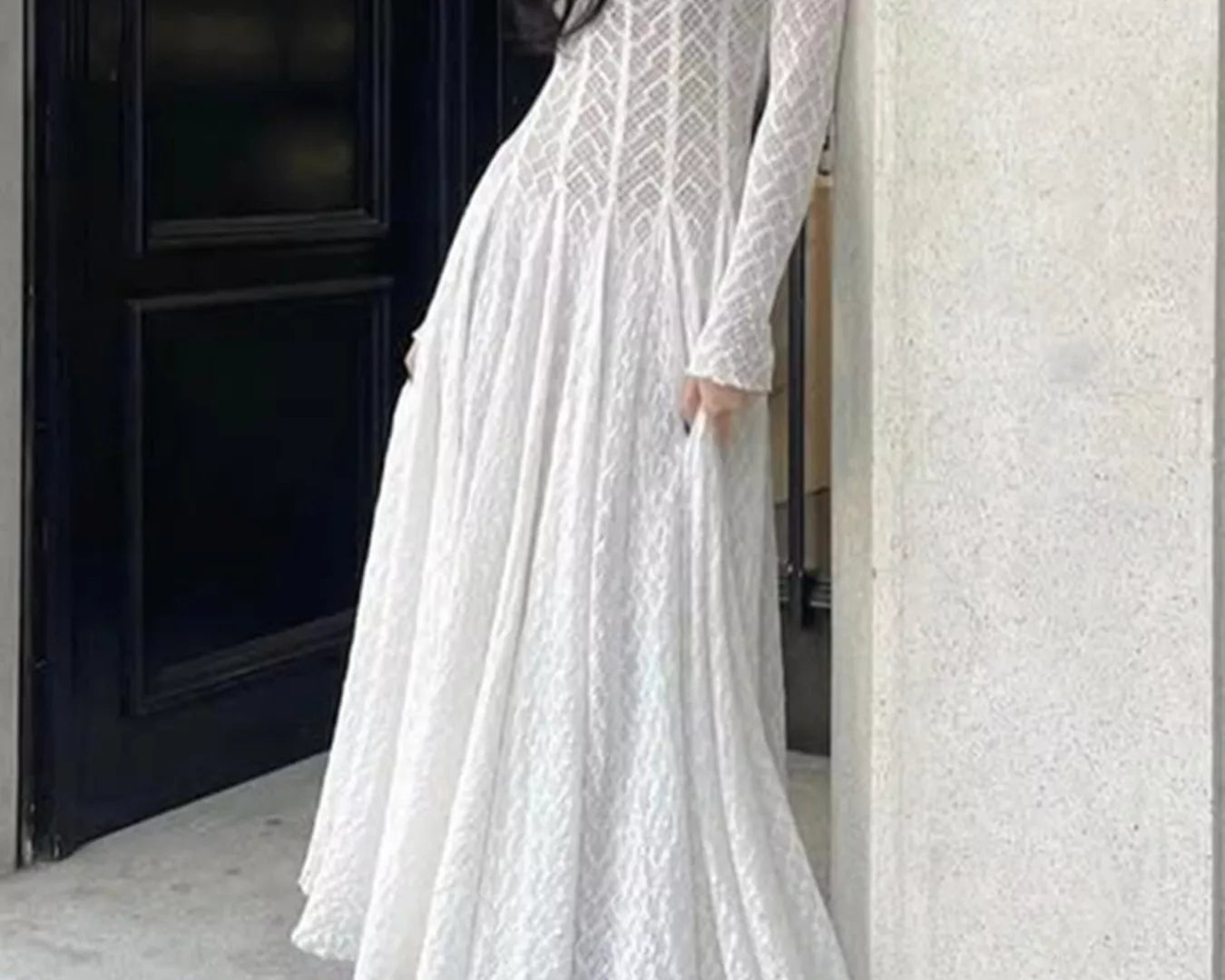 NEWYORKLISTED STYLE COLLECTION: Woman wearing a white lace dress standing against a building entrance.