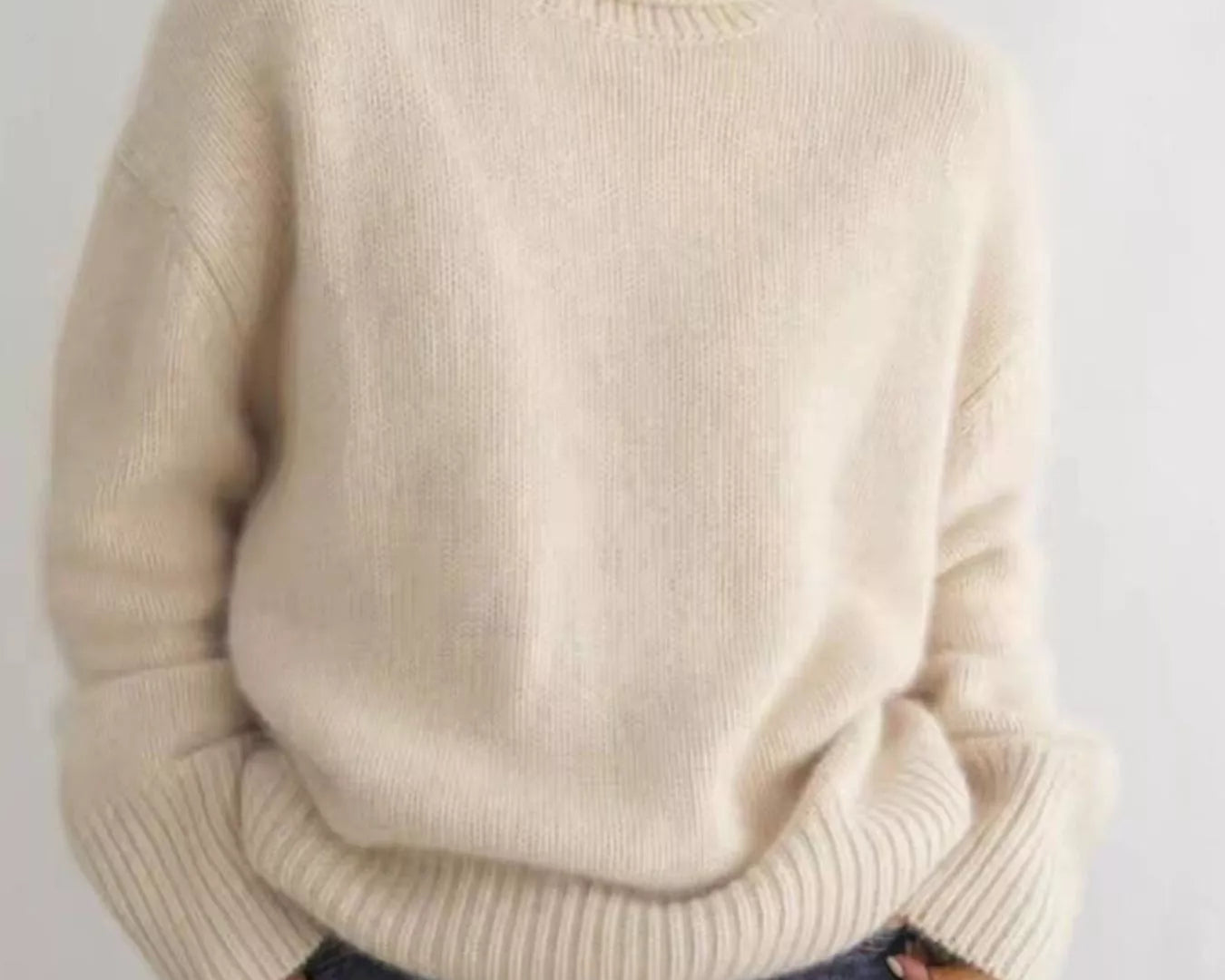 Person wearing a beige sweater and blue jeans against a plain background NEWYORKLISTED STYLE COLLECTION