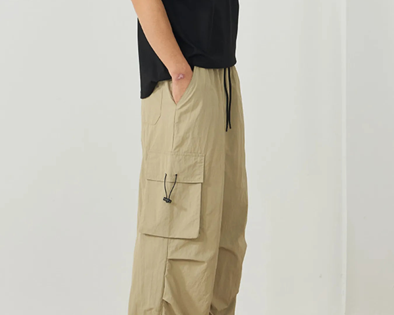 NEWYORKLISTED ATLAS MEN's Collection: Person wearing beige cargo pants and a black top against a white background