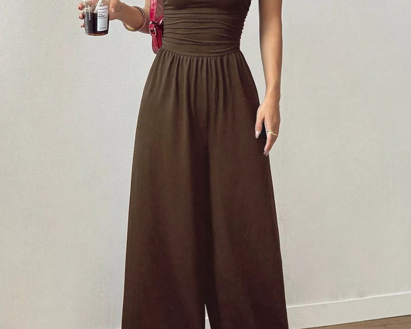 NEWYORKLISTED Comfort Collection: Woman wearing a brown jumpsuit holding a drink against a plain background