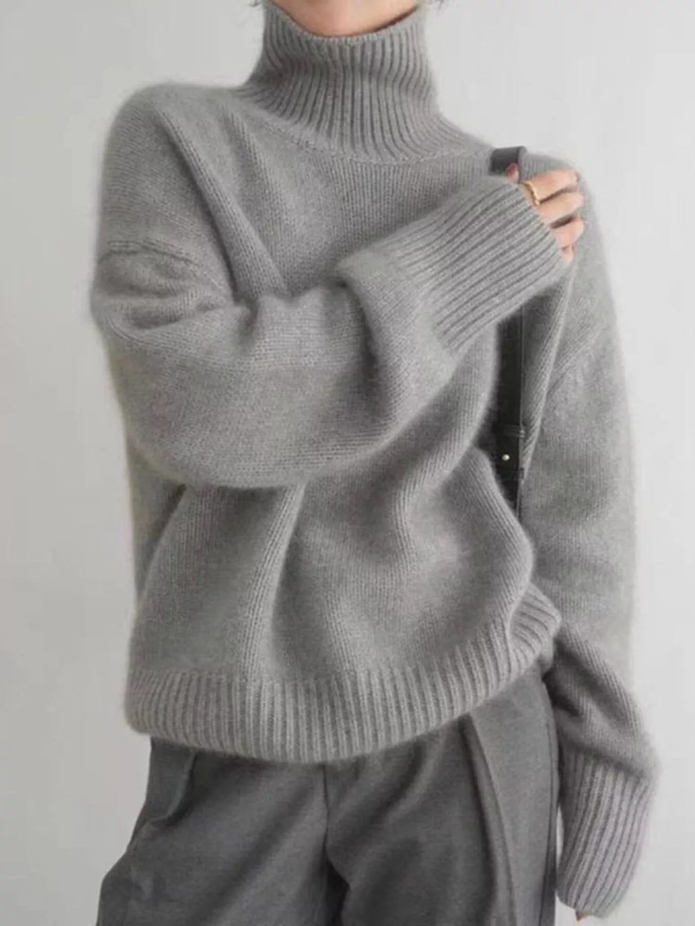 Person wearing a gray turtleneck sweater against a plain background