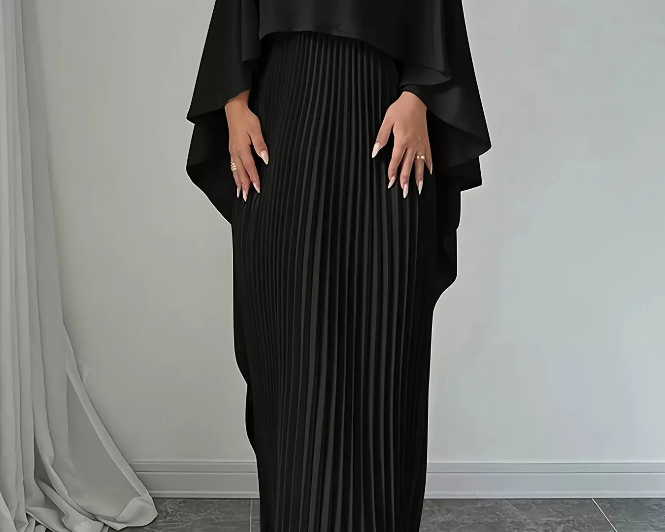 NEWYORKLISTED STYLE COLLECTION: Woman wearing a black pleated dress with a draped top against a neutral background