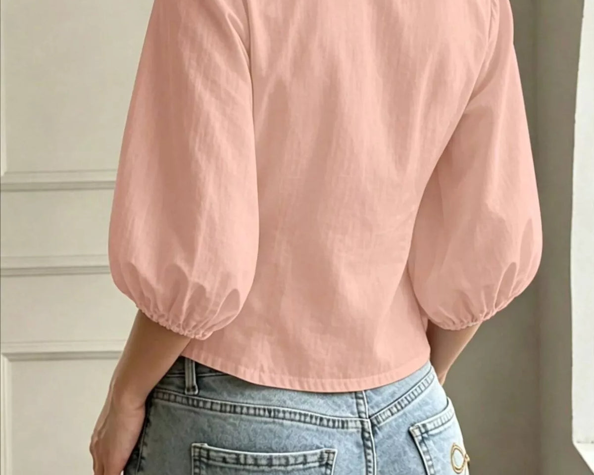 NEWYORKLISTED STYLE COLLECTION: A woman shown from the back wearing a light pink cropped blouse with voluminous elbow-length puff sleeves and light-wash blue jeans with decorative bow embroidery on the back pockets.
