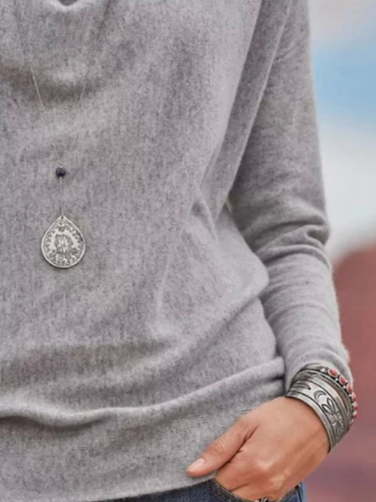 NEWYORKLISTED STYLE COLLECTION: Gray sweater with a decorative button and silver bracelet on a blurred background