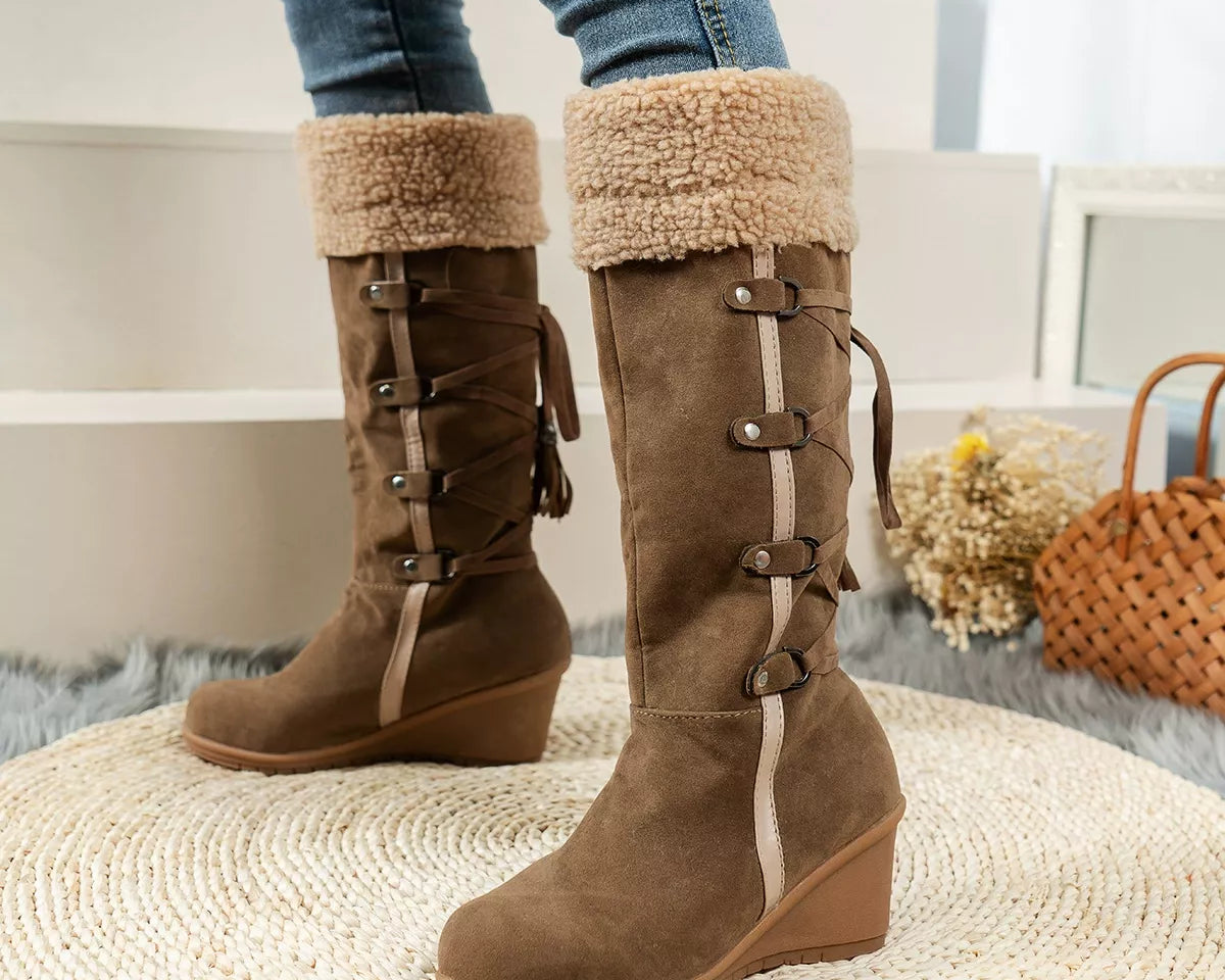 NEWYORKLISTED SHOE COLLECTION: Brown knee-high boots with fur trim worn by a person, sitting on a textured surface.