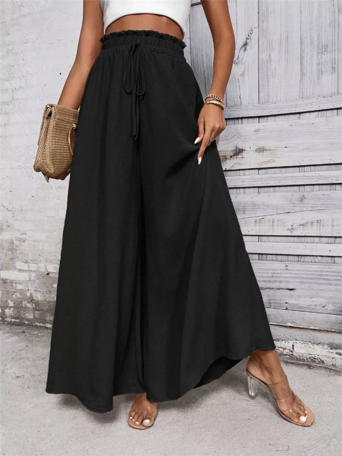 NEWYORKLISTED STYLE COLLECTION: Person wearing black wide-leg pants with a white top against a wooden wall.