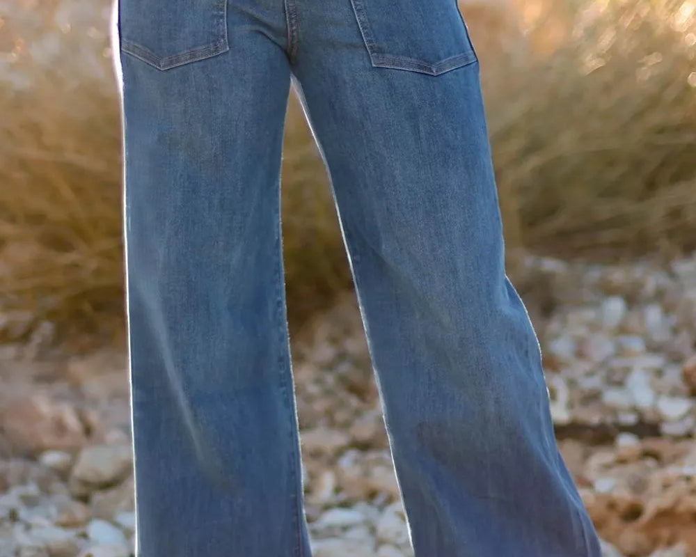 NEWYORKLISTED STYLE COLLECTION: Person wearing blue bell-bottom jeans standing on a rocky surface with a blurred natural background