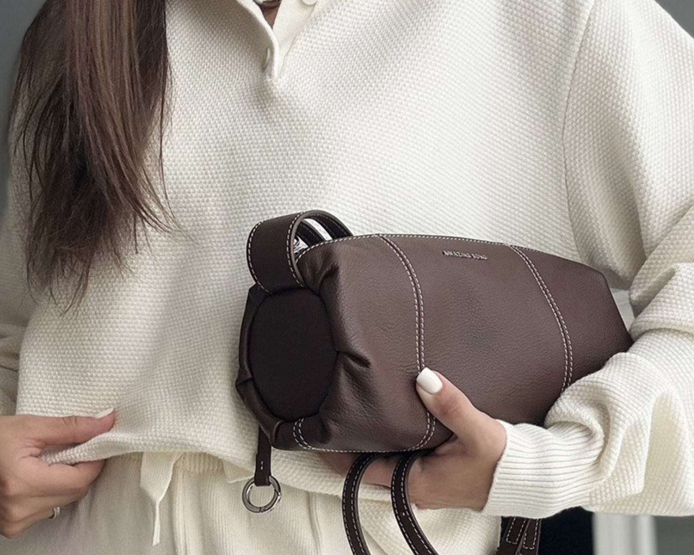 NEWYORKLISTED Comfort Collection: Person holding a brown handbag with a neutral background