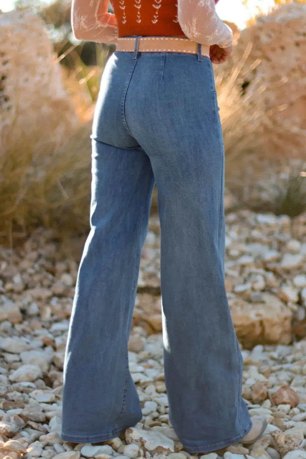 NEWYORKLISTED STYLE COLLECTION: Person wearing blue flared jeans standing on a rocky surface with a blurred natural background