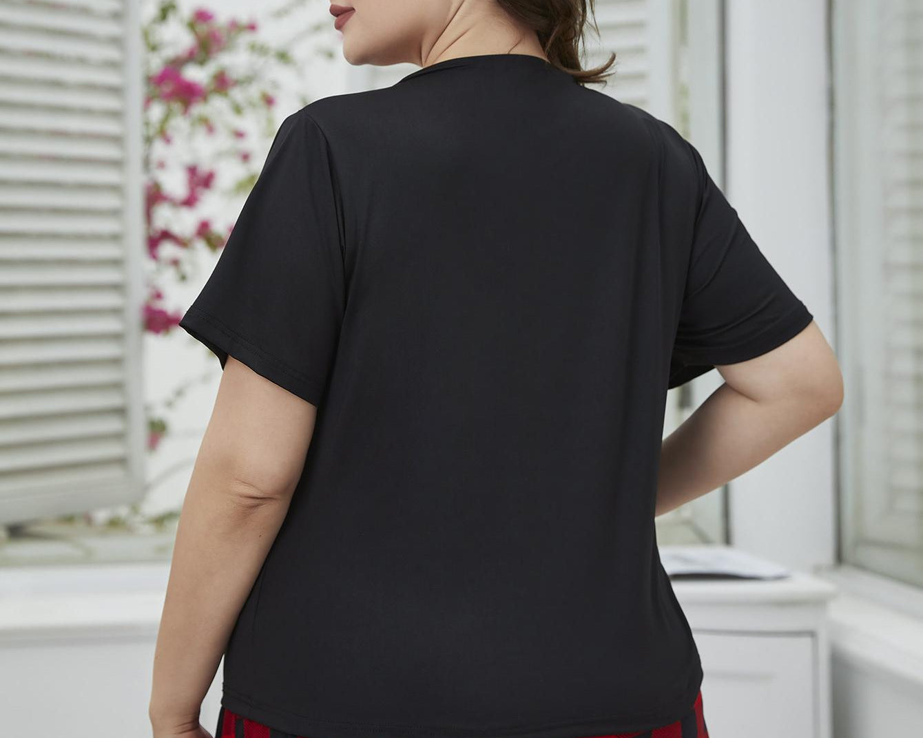 NEWYORKLISTED Intimate Apparel: Woman wearing a black t-shirt and red plaid shorts in a room with white walls and floral decorations.