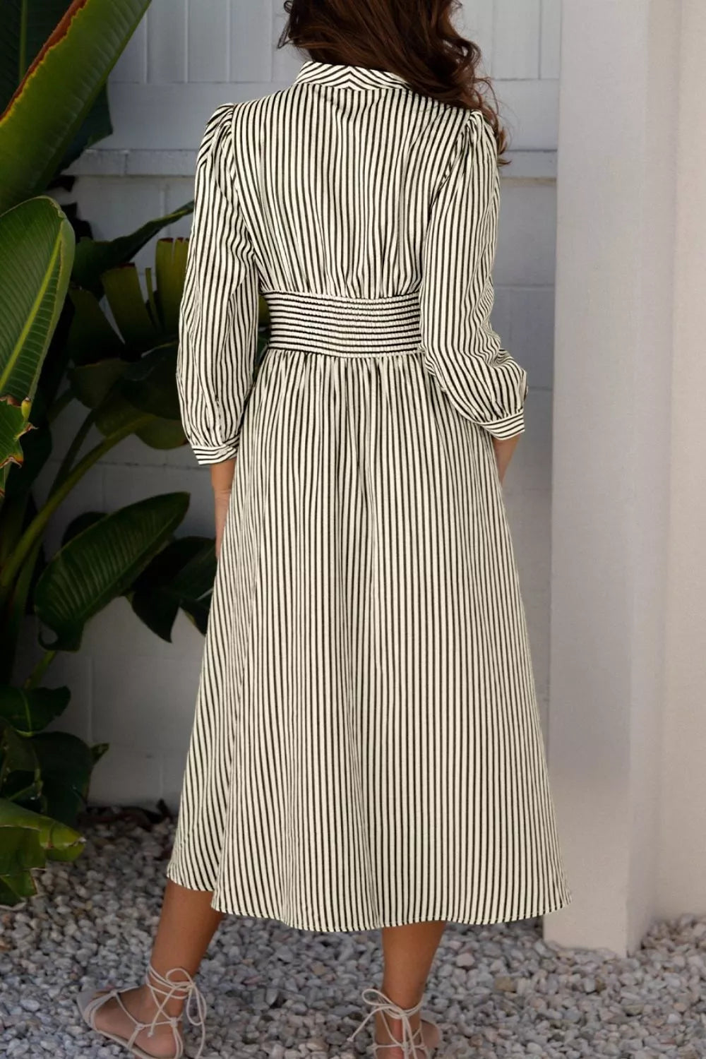 NEWYORKLISTED STYLE COLLECTION: Woman wearing a striped dress standing in a room with plants.