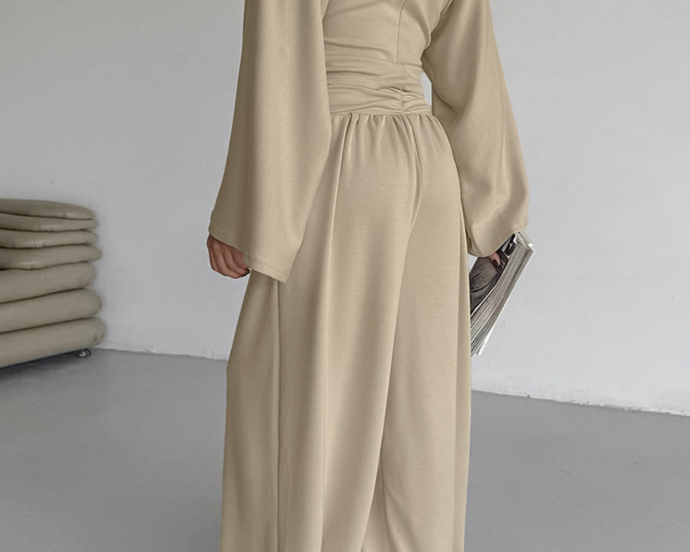 NEWYORKLISTED STYLE COLLECTION: Person wearing a beige jumpsuit in a minimalistic room.