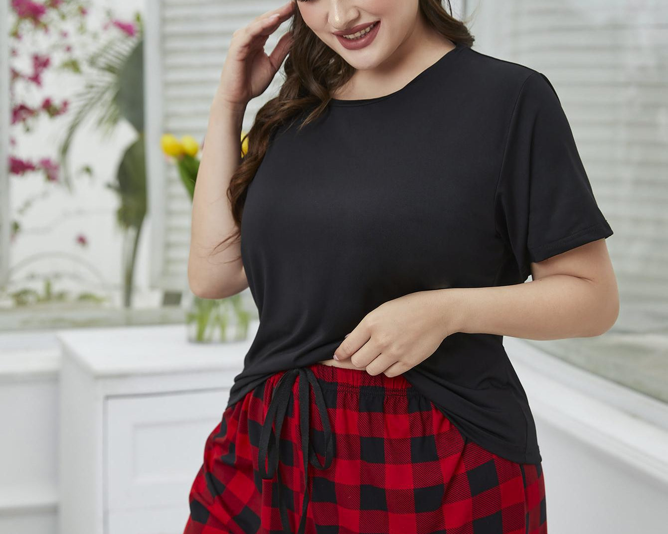 NEWYORKLISTED Intimate Apparel: Woman wearing a black t-shirt and red plaid shorts in a bright room.