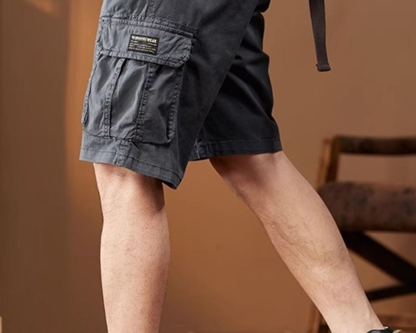 NEWYORKLISTED ATLAS MEN's COLLECTION: Person wearing gray cargo shorts with a brown backpack indoors.
