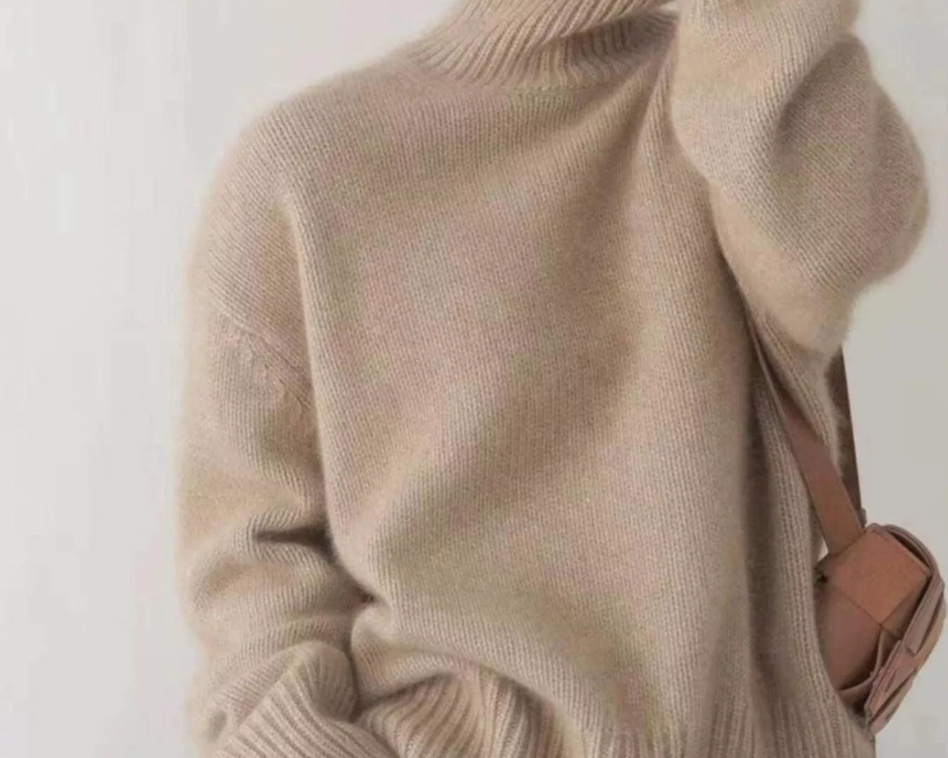 Person wearing a beige turtleneck sweater with a plain background