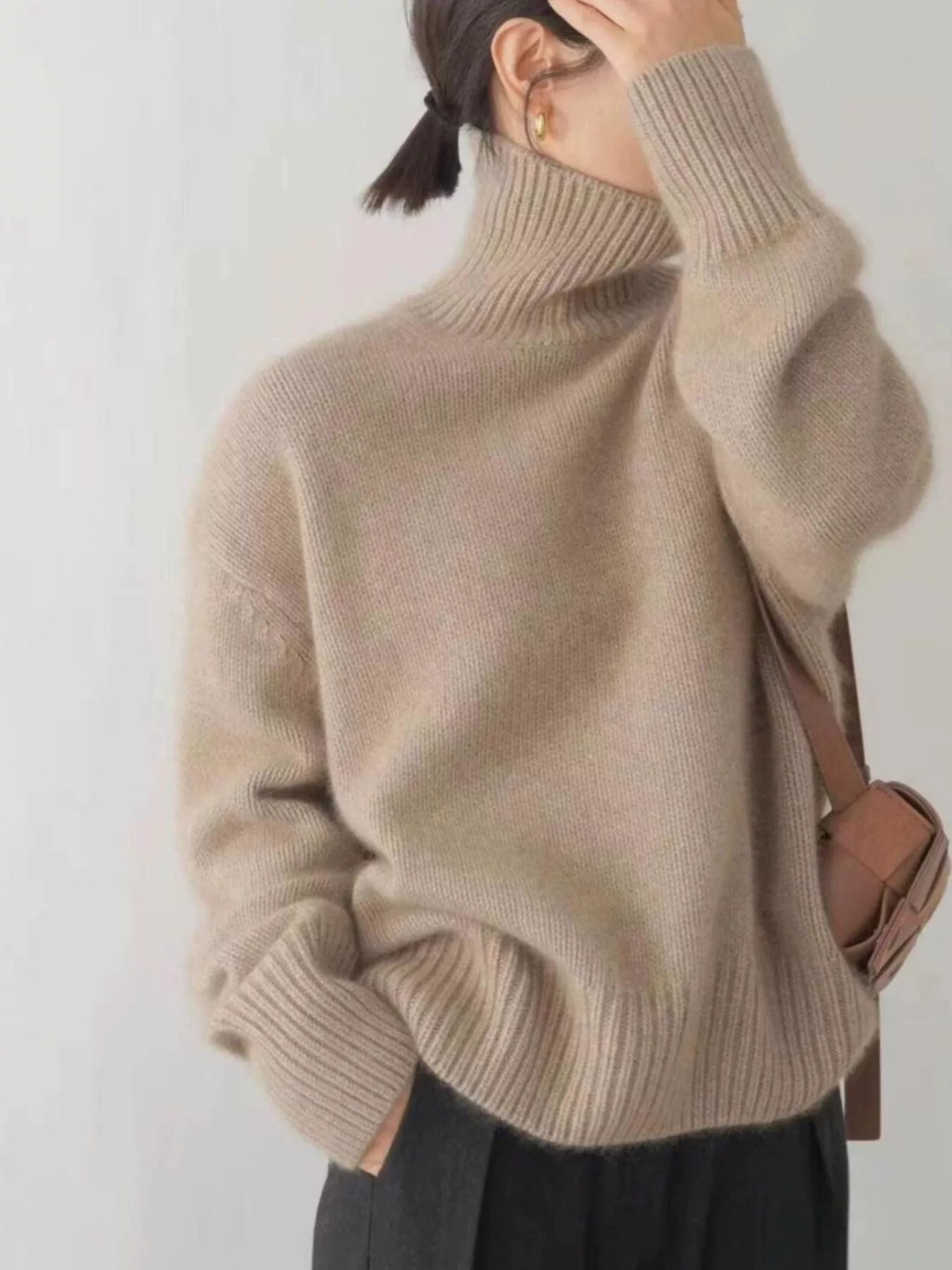 Person wearing a beige turtleneck sweater with a plain background