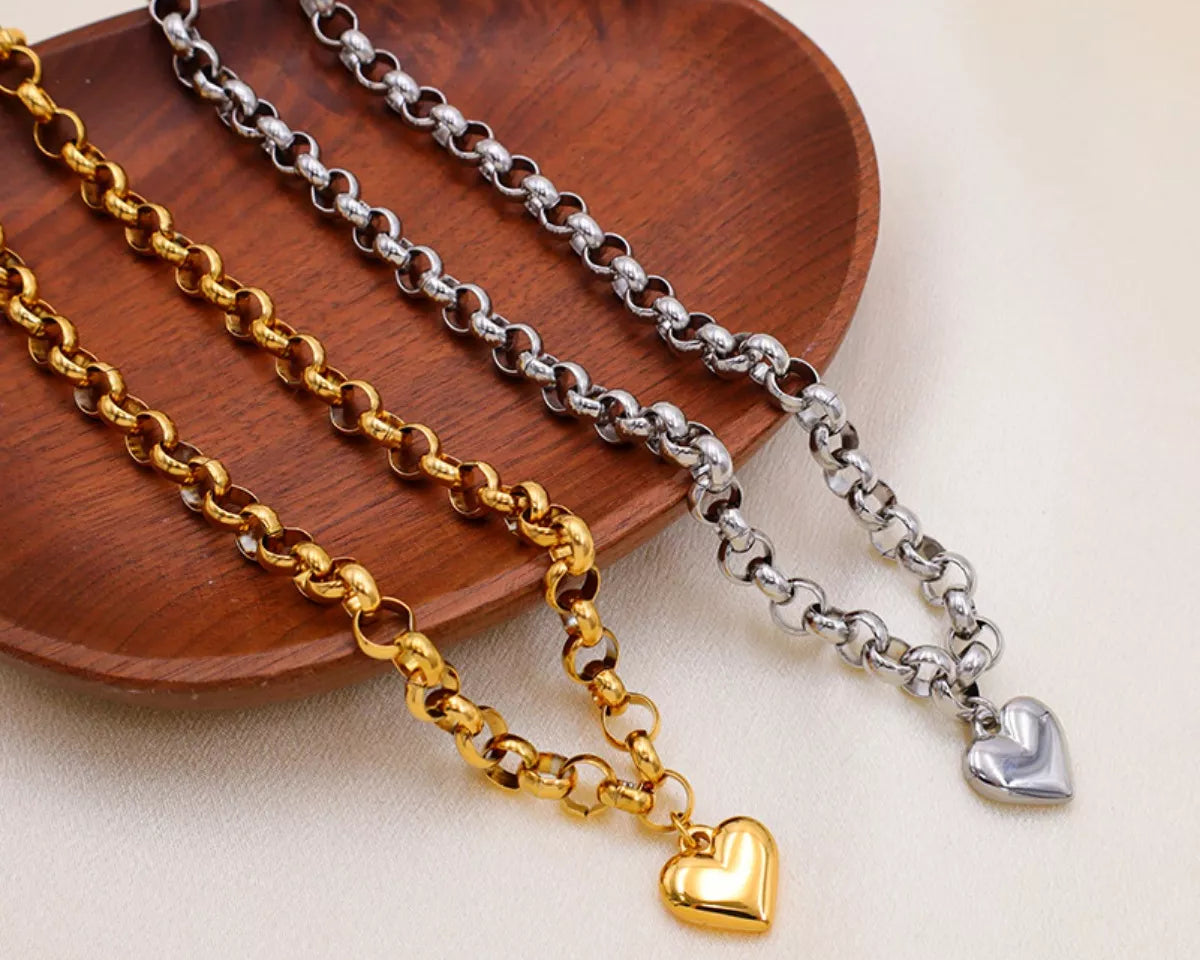 NYLD Glamour Collection by NEWYORKLISTED: Three gold and silver chain necklaces with heart pendants on a wooden plate.