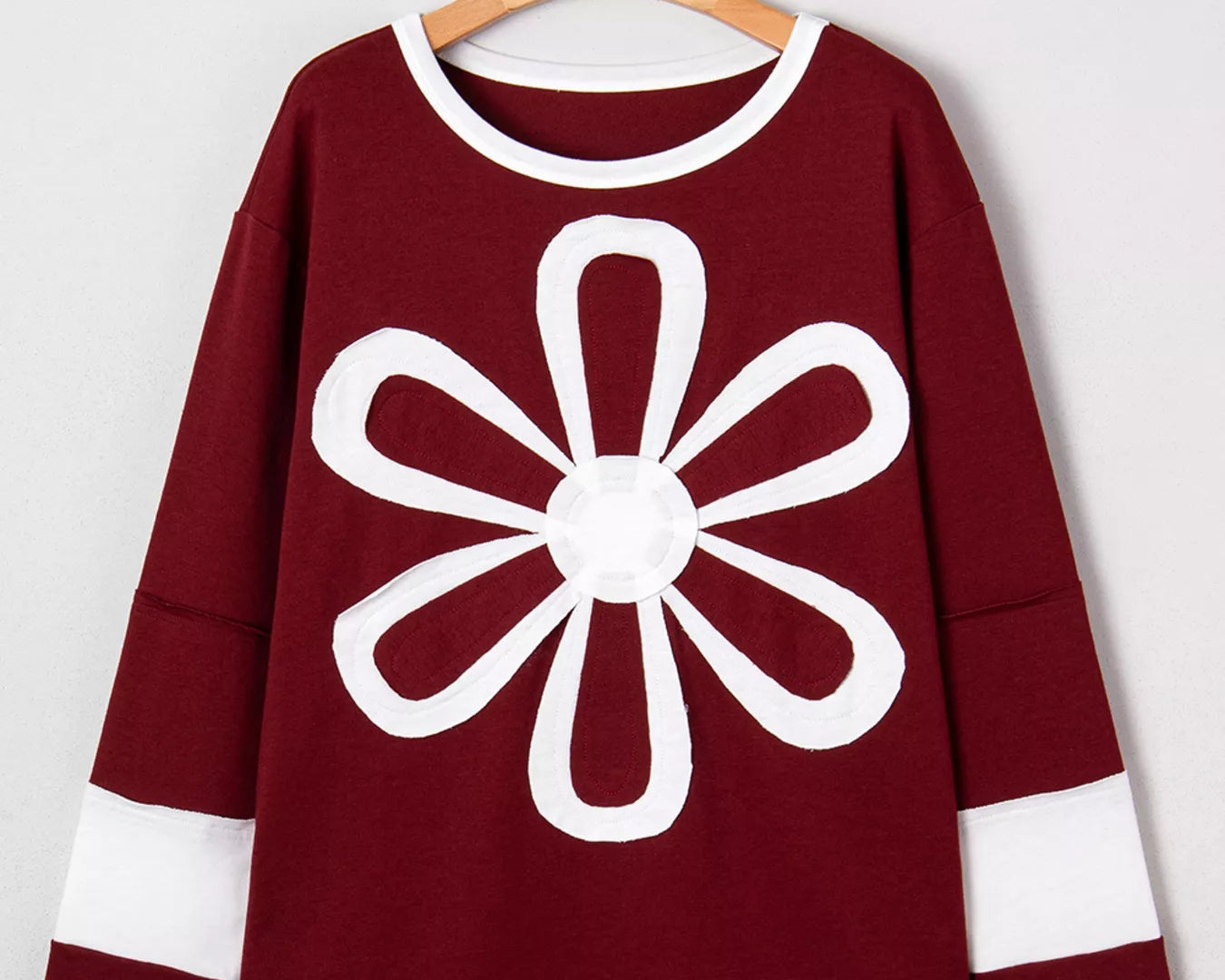 NEWYORKLISTED STYLE COLLECTION: Maroon sweater with a white flower design on a hanger against a white background