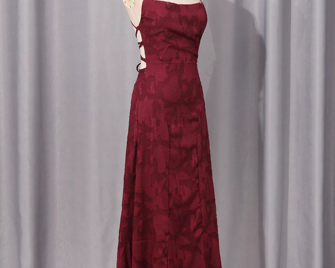 NEWYORKLISTED STYLE COLLECTION: Burgundy evening gown on a mannequin against a gray curtain background