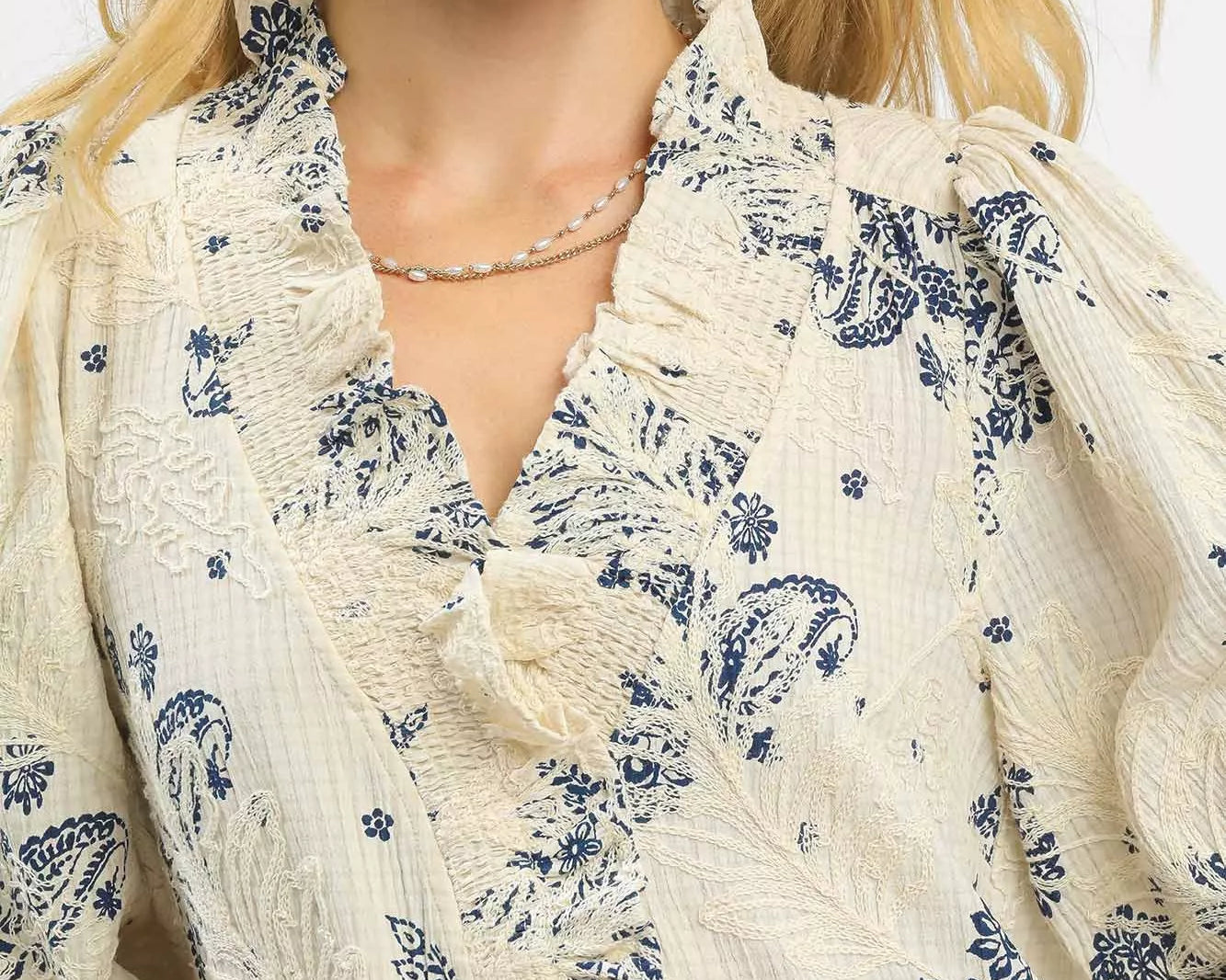 NEWYORKLISTED STYLE COLLECTION: Woman wearing a cream-colored blouse with blue floral patterns on a white background
