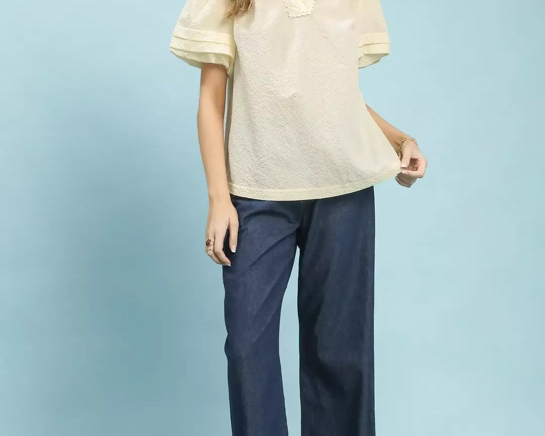 NEWYORKLISTED Style Collection: Woman wearing a cream blouse and navy pants on a light blue background