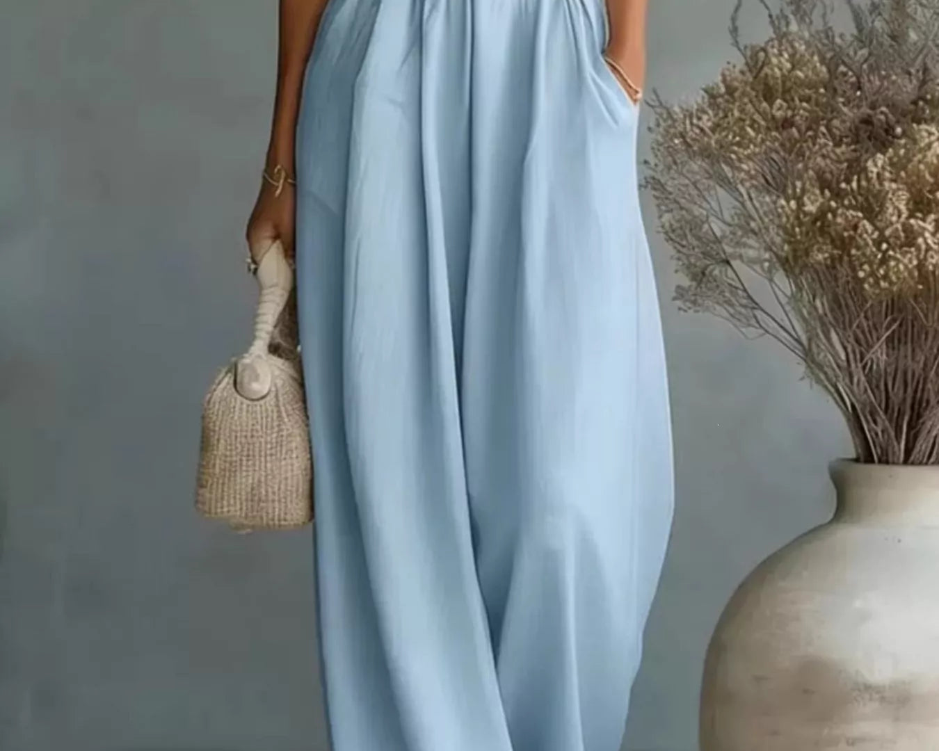 NEWYORKLISTED STYLE COLLECTION: Woman wearing a light blue dress holding a small bag, standing next to a vase with dried flowers.