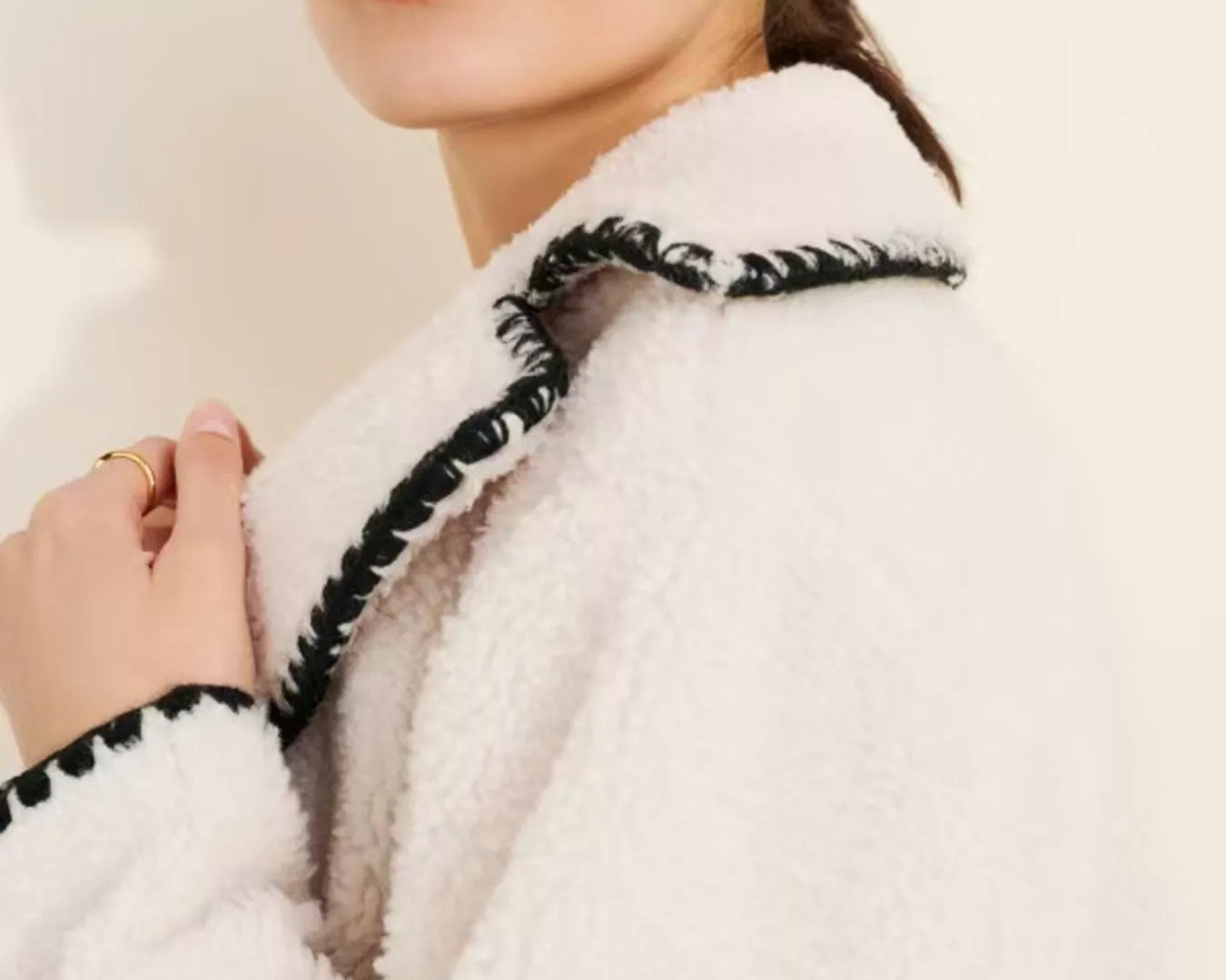 NEWYORKLISTED STYLE COLLECTION: Close-up of a person wearing a white coat with black trim against a plain background