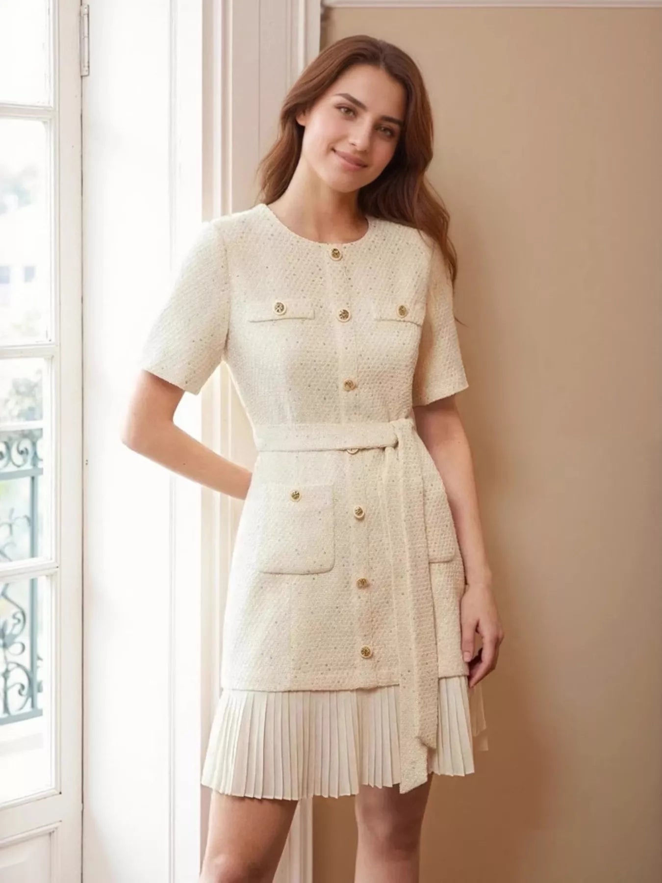 NEWYORKLISTED STYLE COLLECTION: Woman wearing a cream-colored dress with buttons standing in a room with a window.