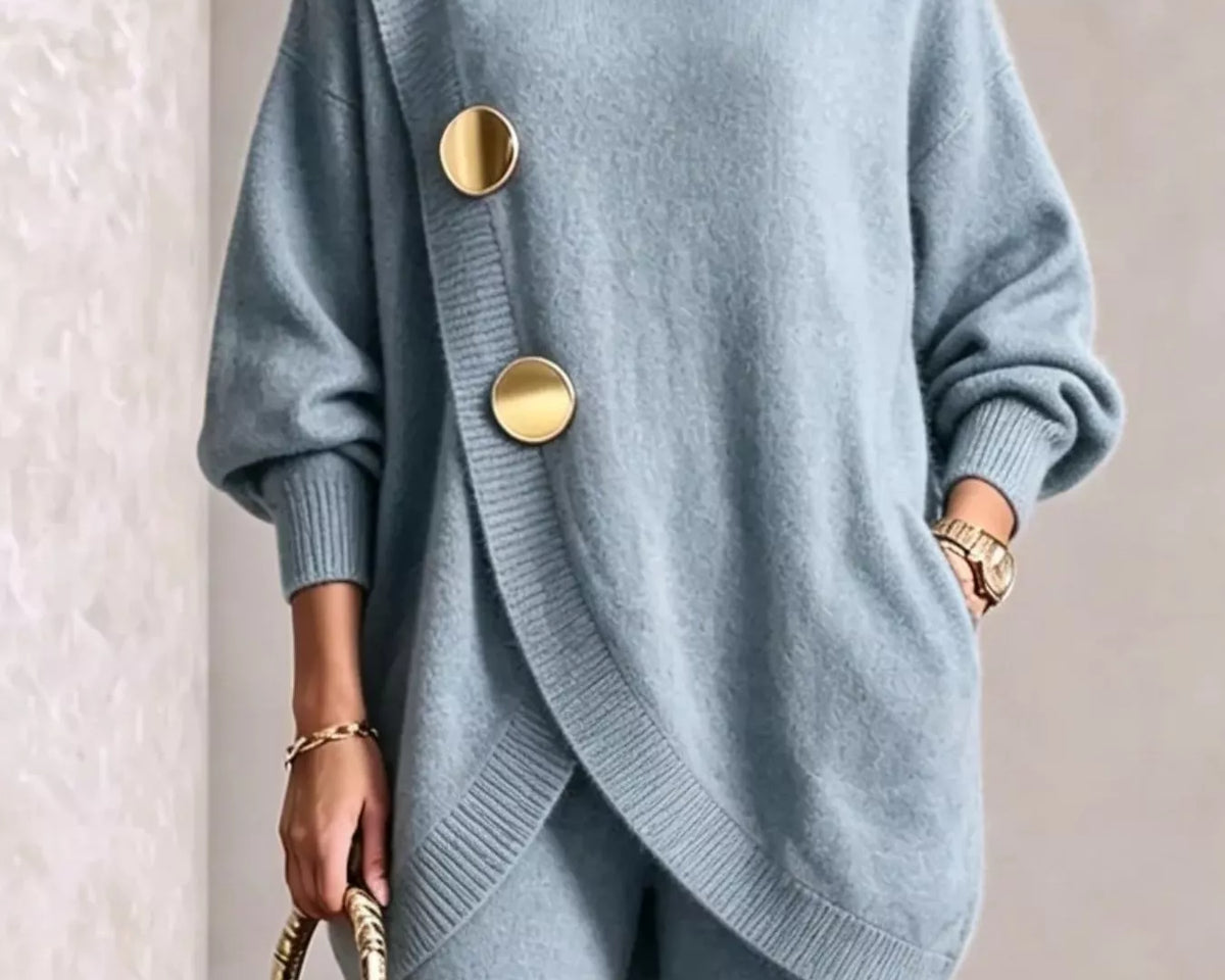NEWYORKLISTED STYLE COLLECTION: A woman wearing a light blue knit turtleneck sweater with oversized gold buttons and matching knit pants, holding a small metallic gold handbag against a neutral indoor background.
