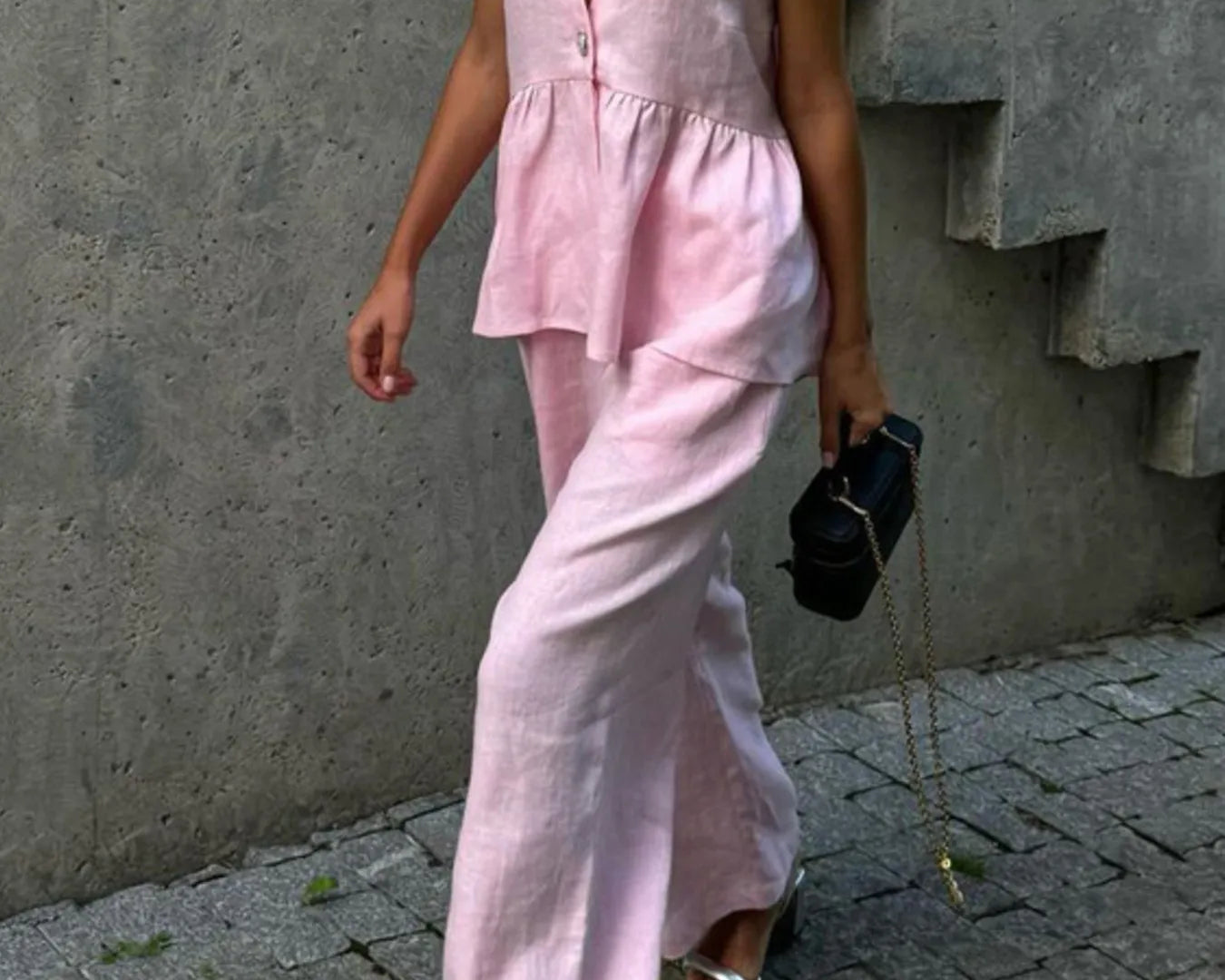 Person wearing a NEWYORKLISTED Style Model wearing pink sleeveless top and pants against a concrete wall.