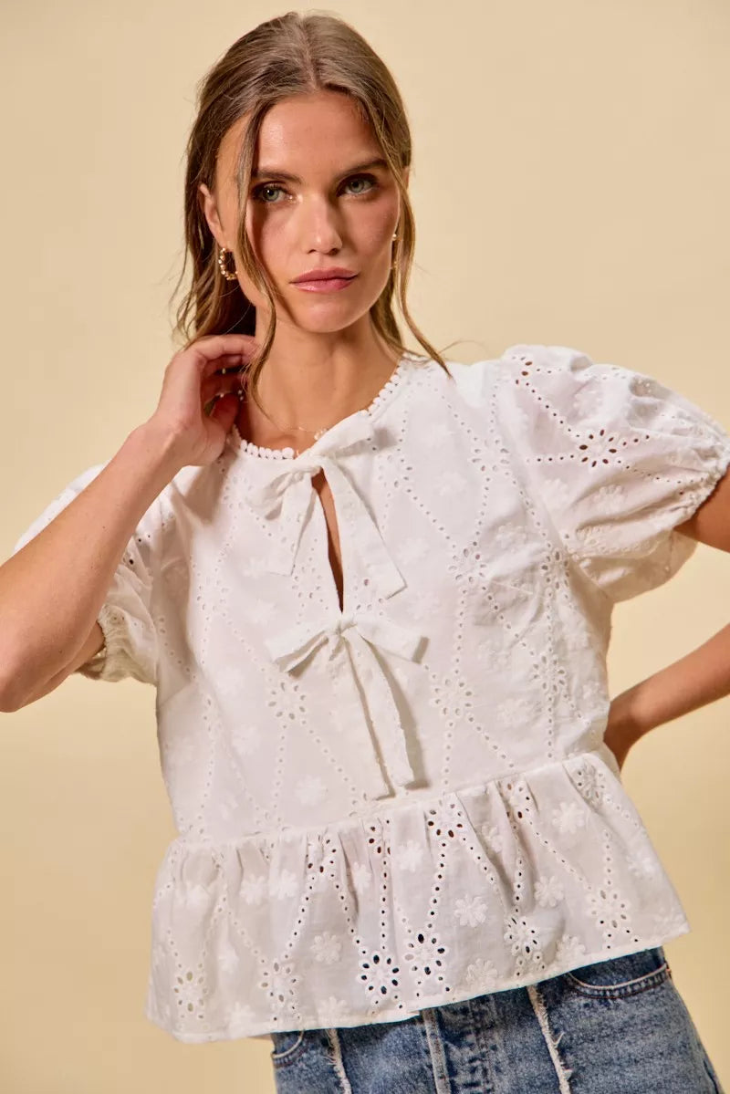 NEWYORKLISTED STYLE COLLECTION: Woman wearing a white embroidered blouse with blue jeans on a beige background