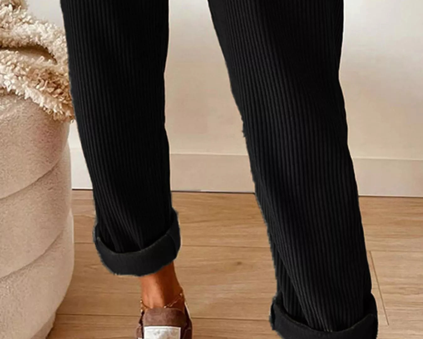 Person wearing black ribbed pants with white sneakers on a wooden floor.