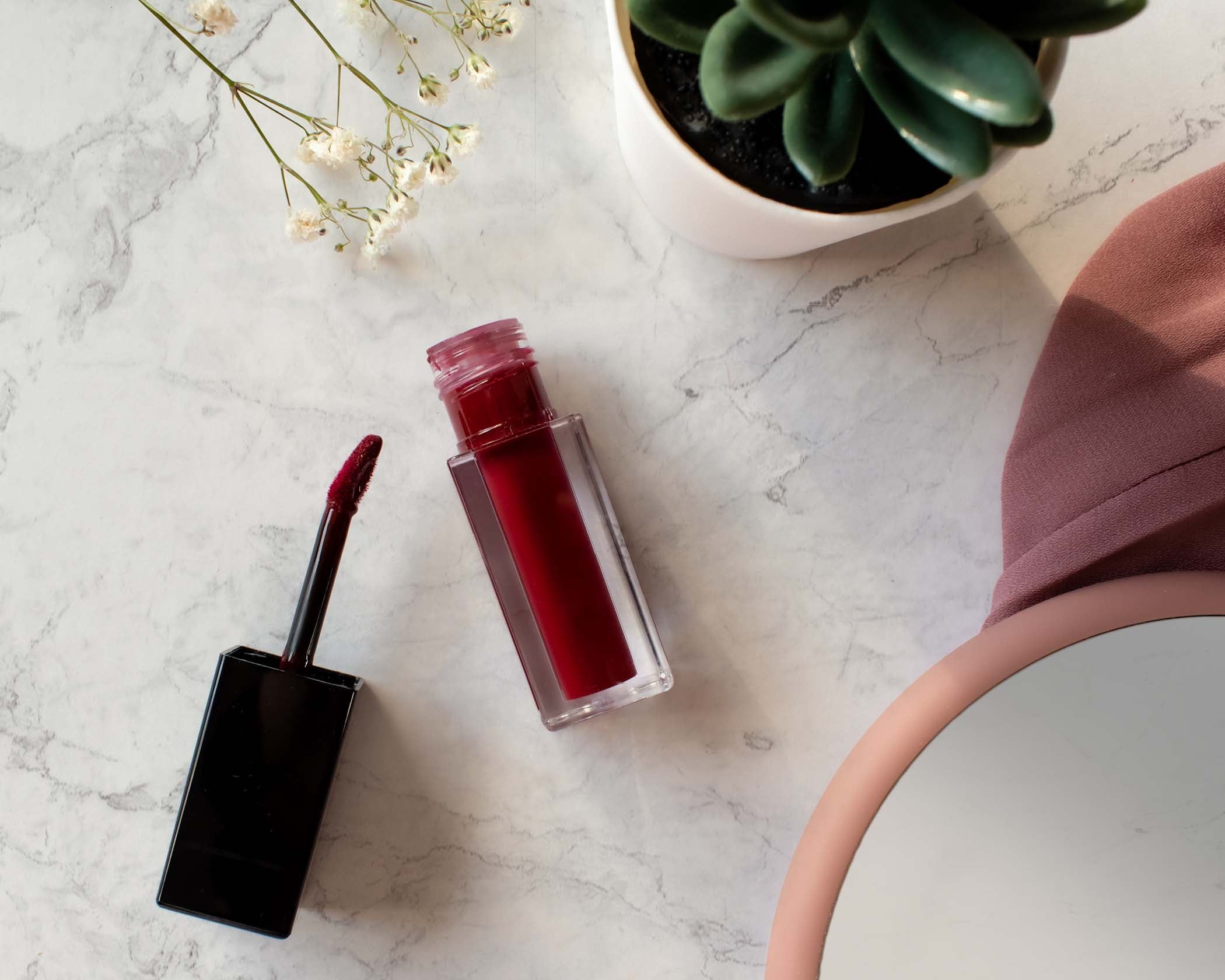 NEWYORKLISTED Cosmetic Collection: Red lip stain and applicator on a marble surface with a plant in the background