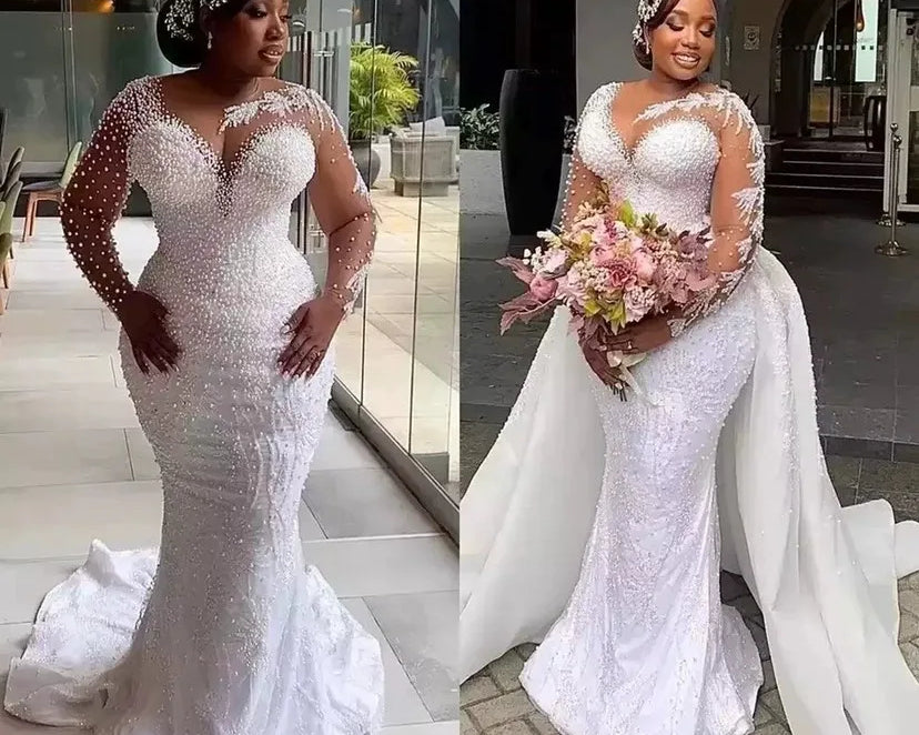 Woman in a white beaded wedding dress holding flowers indoors.